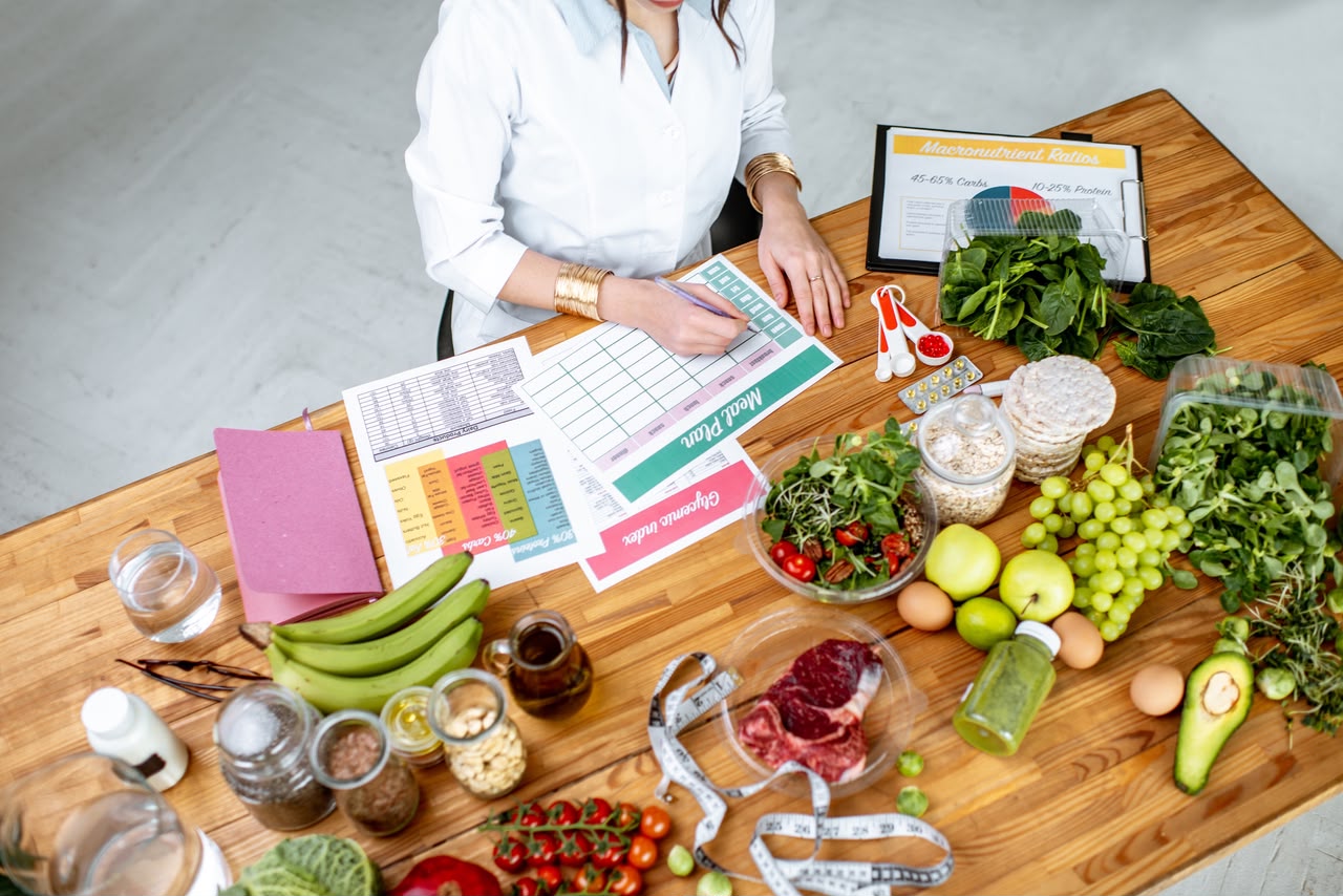 Training vs nutrition: a coach reviewing a meal plan chart at a table surrounded by whole foods